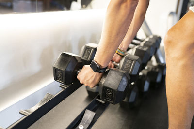 Anonymous person with smart watch taking heavy dumbbells from rack during weightlifting workout in gym