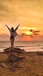 Rear view of carefree seductive woman with arms raised looking at sea against sky during sunset