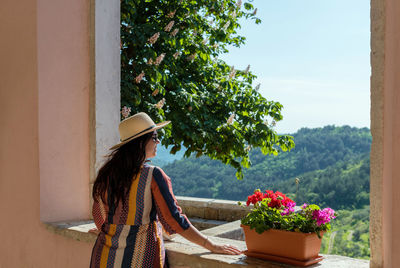 Rear view of woman standing on terrace of old building, looking at beautiful landscape in summer