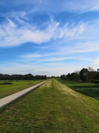 Empty road amidst field against sky