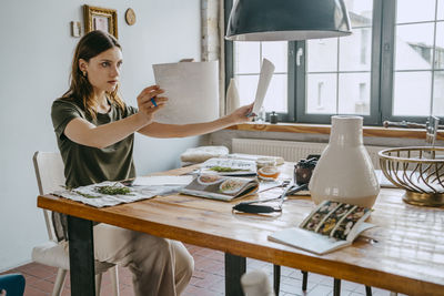 Concentrated female food stylist comparing photographs sitting at table in studio