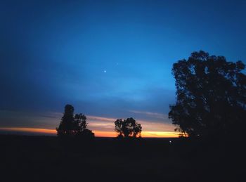 Silhouette trees on landscape against sky at sunset