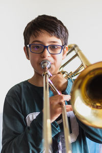 Portrait of cute boy playing trumpet against wall