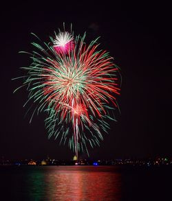 Low angle view of illuminated fireworks over lake against sky at night