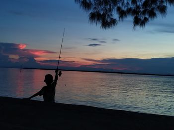 Silhouette man fishing in sea against sky during sunset