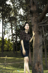 Portrait of young woman standing by tree trunk in forest