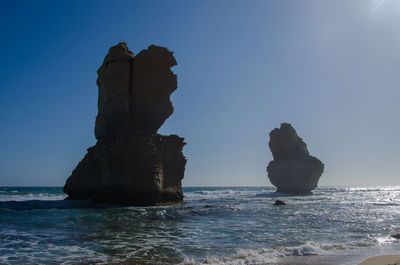 Rock formation in sea against clear blue sky