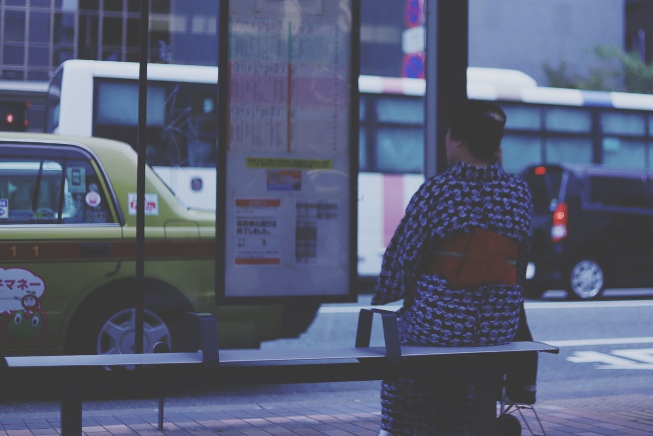 mode of transportation, real people, transportation, land vehicle, rear view, one person, motor vehicle, city, car, women, public transportation, bus, standing, street, architecture, lifestyles, adult, focus on foreground, day, warm clothing