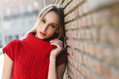 Portrait of beautiful woman standing by brick wall