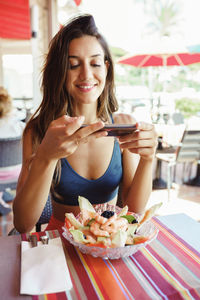 Young woman photographing food with phone on table at restaurant