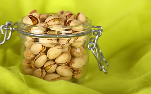 Close-up of pistachios in jar on green fabric