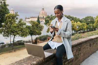 Girl with laptop using smart phone on wall