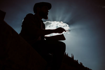 Side view of silhouette man sitting against sky