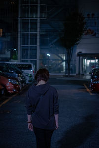 Rear view of woman standing on illuminated street at night