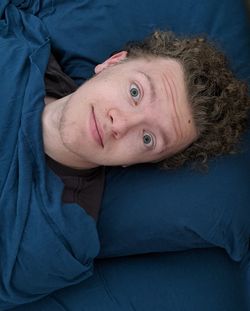 Portrait of teenage boy with curly hair lying down on bed with eyes wide open