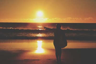 Silhouette woman standing on beach against sky during sunset