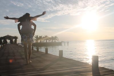 Rear view of man piggybacking woman on pier over during sunny day