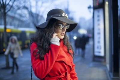 Young woman wearing warm clothing while answering smart phone in city