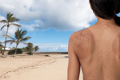 Rear view of woman standing at beach against sky