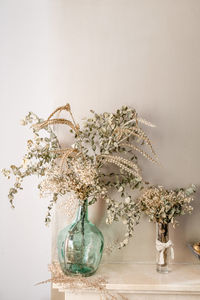 Glass vases with dried plants and branches covered with leaves decorating room of home