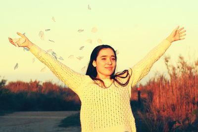 Portrait of young woman with arms raised against sky