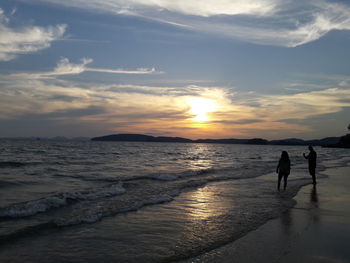 Silhouette people at beach against sky during sunset