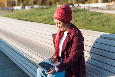 Rear view of woman using laptop while sitting on railroad track