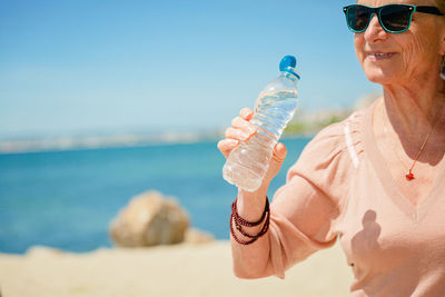 Senior woman sitting on the beach with a bottle of water