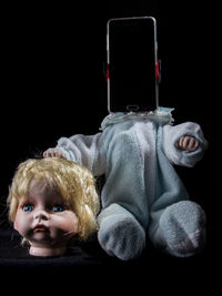 Close-up of broken doll with mobile phone against black background