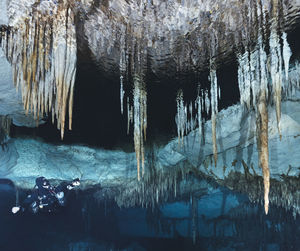 Low angle view of man scuba diving below stalactites in sea