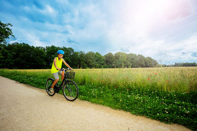 Rear view of man riding bicycle on field against sky