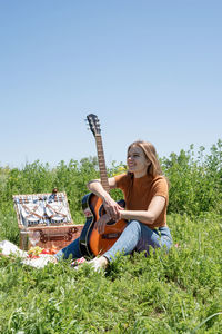 Young woman sitting on grassy field against clear sky