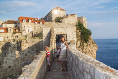 People on wall by sea against sky