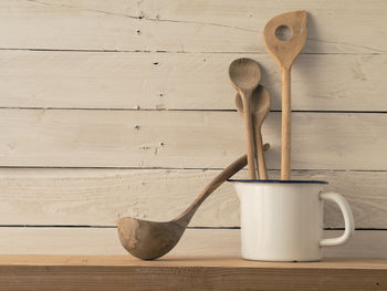 Wooden spoons in container on shelf by wall