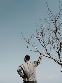 Rear view of man standing by tree against sky