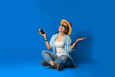 Full length of young woman using smart phone against blue background