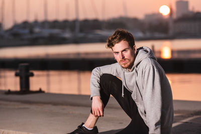 Portrait of young man sitting in city during sunset