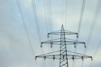 Low angle view of electricity pylon against cloudy sky