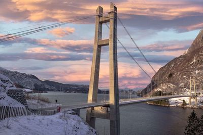 Bridge over snow covered mountains against sky during sunset