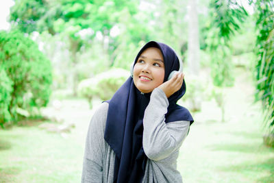 Beautiful young asian muslim woman listening to music with headphones in a park