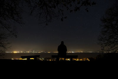 Silhouette man sitting on bench against sky at night