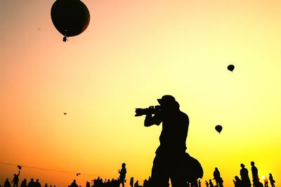 Low angle view of silhouette man photographing against people on field at sunset