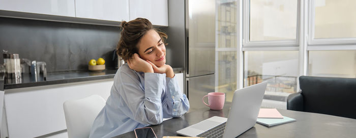 Side view of young woman using laptop at home