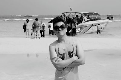 Portrait of young man wearing sunglasses standing against yacht at beach