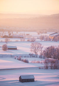 Snow covered landscape against sky during sunset