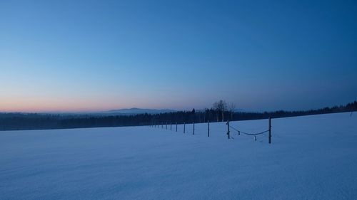 Silhouette trees on snow covered landscape against clear blue sky