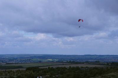 Person paragliding over landscape against sky