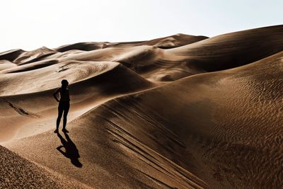 Woman standing on sand dune in desert against clear sky