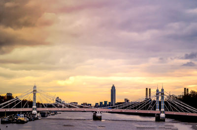 Suspension bridge over river against cloudy sky