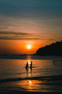 Silhouette people on sea against sky during sunset